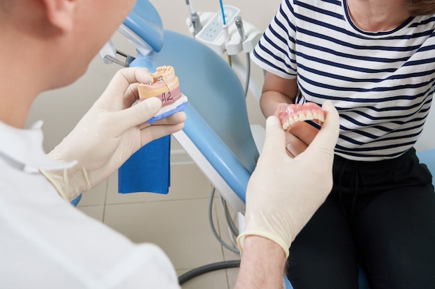 Dentista masculino mostrando a su paciente un implante dental en la clínica moderna