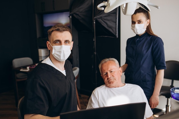 Dentista masculino que usa un taladro dental mientras trabaja en los dientes de un paciente maduro