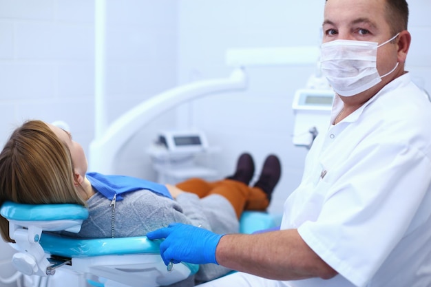 Dentista masculino sênior em consultório odontológico conversando com paciente do sexo feminino e se preparando para tratamento