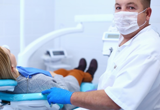 Dentista masculino sênior em consultório odontológico conversando com paciente do sexo feminino e se preparando para tratamento