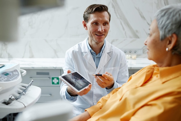 Dentista masculino sorridente segurando tablet digital com imagem de raio x de dentes