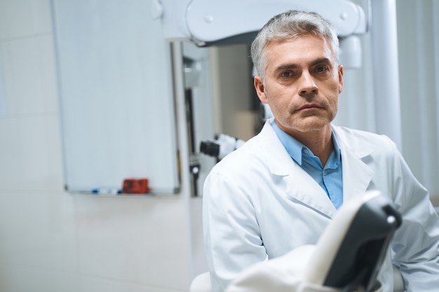 El dentista masculino en uniforme blanco está de pie en la clínica moderna y espera una cita con los pacientes.