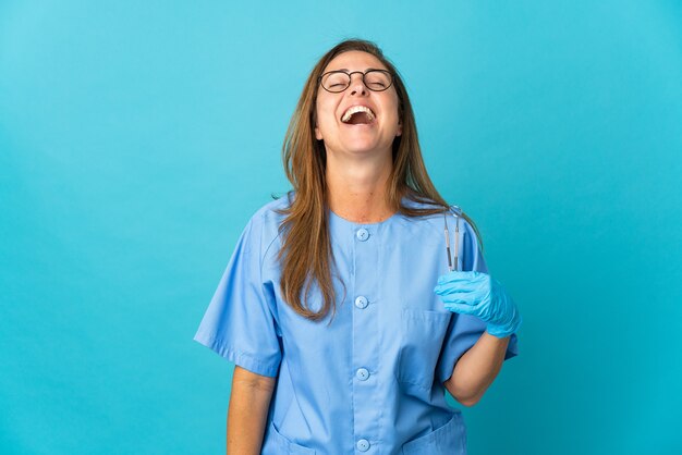 Dentista de mediana edad mujer brasileña sosteniendo herramientas sobre pared aislada riendo