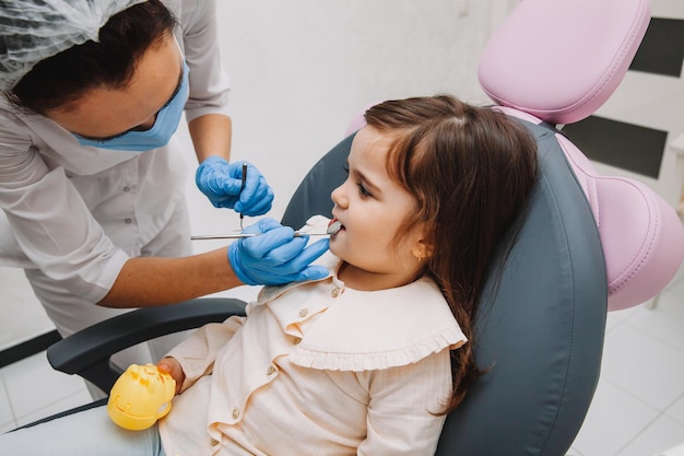 El dentista, el médico examina la cavidad bucal de una niña, utiliza un espejo bucal, primer plano de los dientes de leche, el concepto de odontología pediátrica, tratamiento dental.