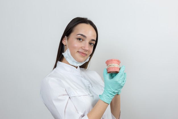 El dentista médico de la muchacha en una bata blanca tiene una simulación de los dientes.