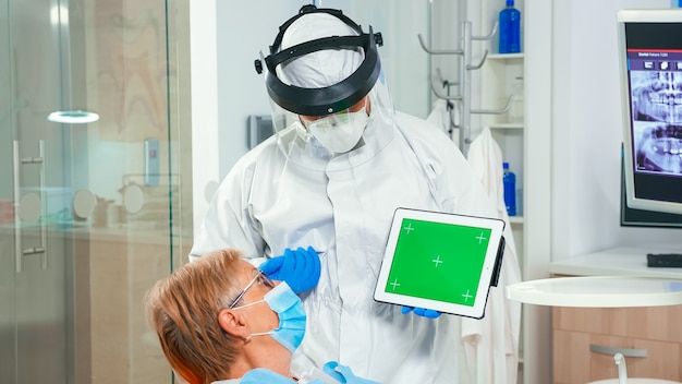 Dentista en mono apuntando a la pantalla verde durante la epidemia de coronavirus. Explicando el uso del monitor con chroma key izolated chroma pc key mockup greenscreen display mock-up touchscreen