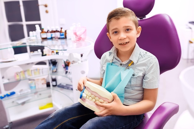 Foto dentista mostra uma dentadura para o menino menino com sorriso muito feliz depois do médico na clínica.