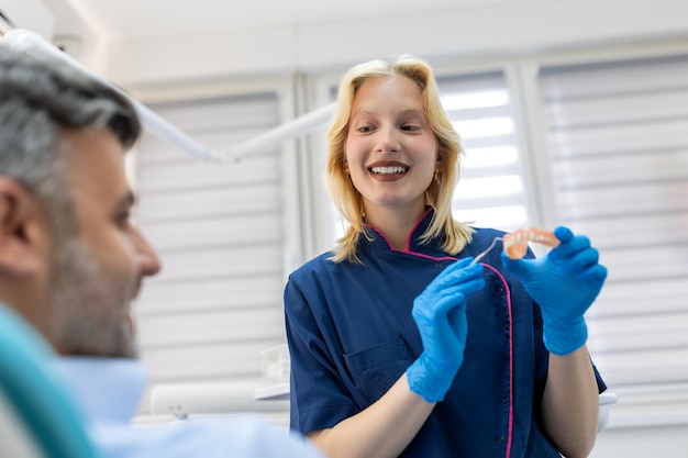Dentista mostrando molde de gesso dental para o paciente Médico dentista mostrando modelo de mandíbula na clínica odontológica conceito de atendimento odontológico Conceito de atendimento odontológico