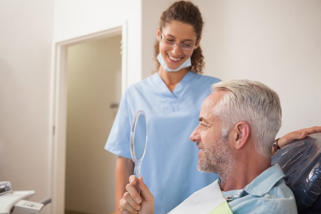 Dentista mostrando paciente seu novo sorriso no espelho