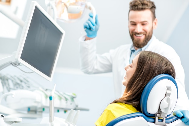 Foto dentista mostrando radiografía de diente paciente joven en el monitor en el consultorio dental