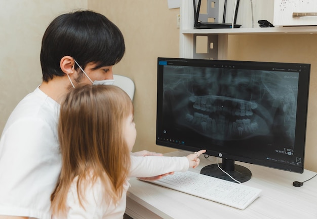 El dentista le muestra al paciente una niña una radiografía de los dientes en la computadora