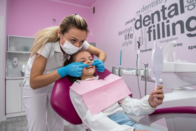 Una dentista muestra los dientes tratados a la pequeña paciente frente al espejo