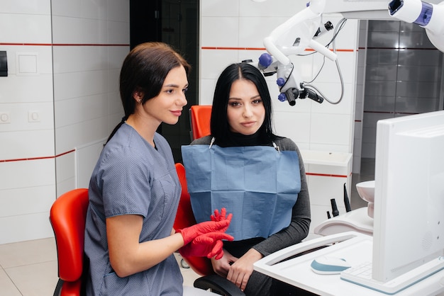 El dentista muestra una imagen de los dientes del paciente y le indica el tratamiento necesario. Odontología, salud.