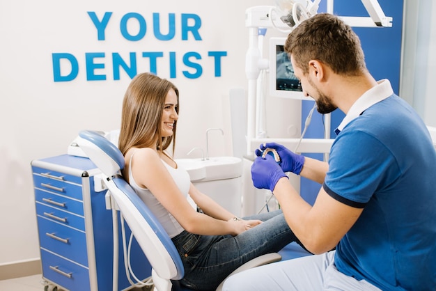 Foto un dentista muestra a la paciente un modelo cerámico de dientes y le explica sobre el trabajo