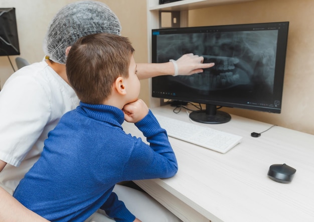 El dentista muestra la radiografía de los dientes en la computadora al niño paciente