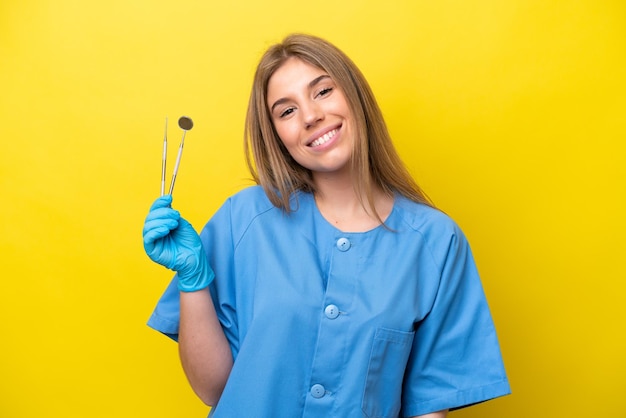 Dentista mujer caucásica sosteniendo herramientas aisladas sobre fondo amarillo pensando en una idea mientras mira hacia arriba