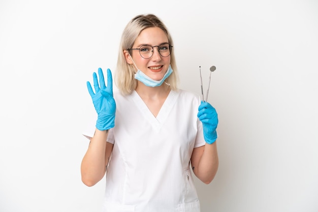 Dentista mujer caucásica sosteniendo herramientas aisladas sobre fondo blanco feliz y contando cuatro con los dedos