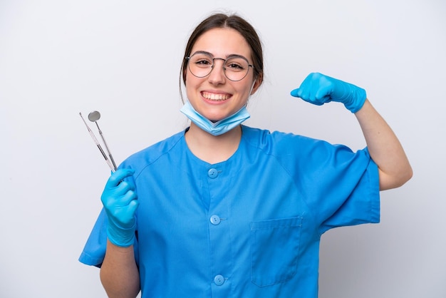 Dentista mujer caucásica sosteniendo herramientas aisladas sobre fondo blanco haciendo un gesto fuerte