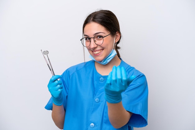 Dentista mujer caucásica sosteniendo herramientas aisladas sobre fondo blanco invitando a venir con la mano Feliz de que hayas venido