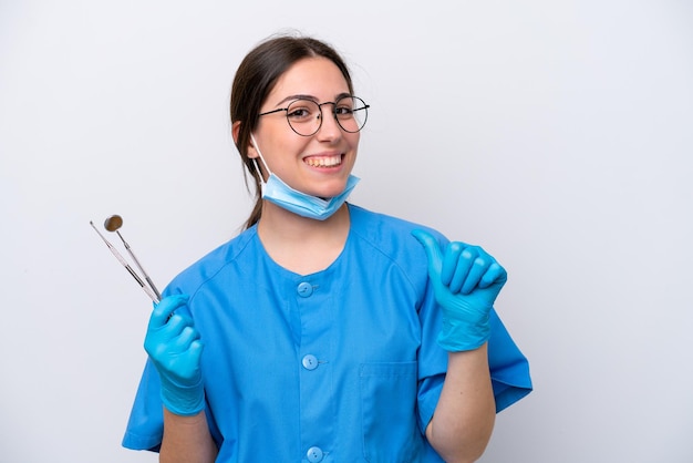 Dentista mujer caucásica sosteniendo herramientas aisladas sobre fondo blanco orgullosa y satisfecha