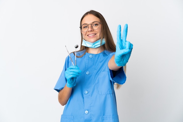 Dentista mujer lituana sosteniendo herramientas sobre pared aislada sonriendo y mostrando el signo de la victoria