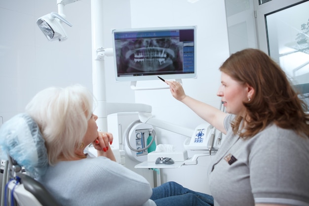 Dentista mujer mostrando escaneo de rayos x dental a su paciente senior