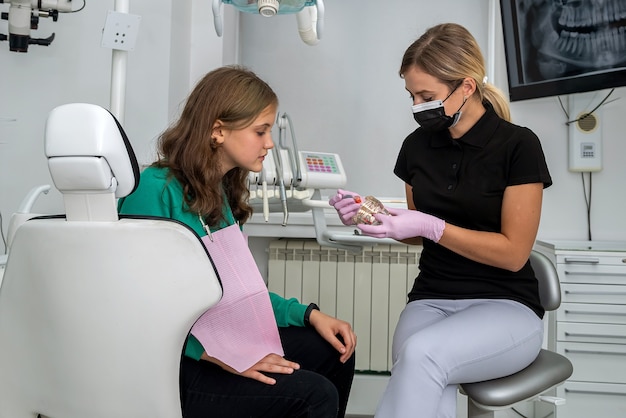 Dentista mujer mostrando mandíbula con dientes para decirle a la niña