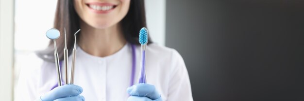 Dentista mujer sonriente sosteniendo la herramienta y el cepillo de dientes en sus manos