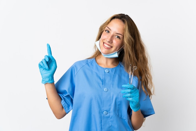 Dentista mujer sosteniendo herramientas aisladas en la pared blanca mostrando y levantando un dedo en señal de lo mejor