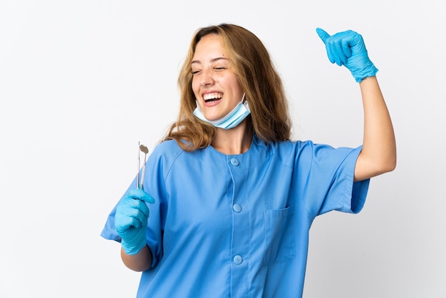 Dentista mujer sosteniendo herramientas aisladas sobre pared blanca celebrando una victoria