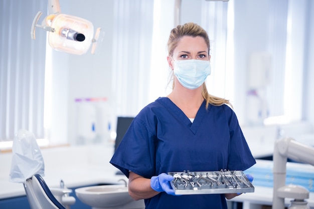 Dentista na máscara segurando bandeja de ferramentas