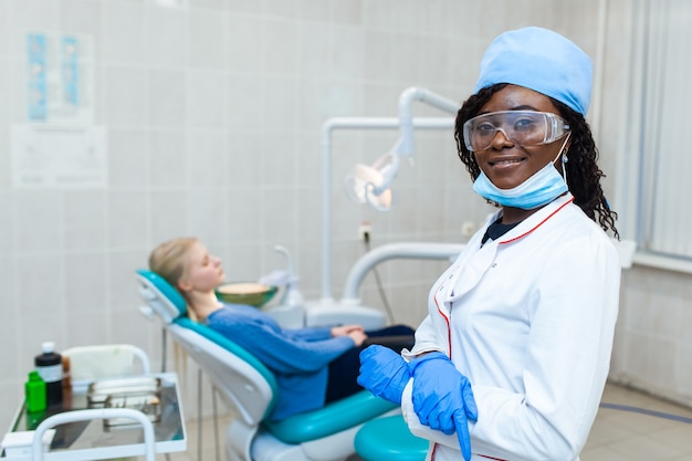 Dentista negro feminino no consultório odontológico, conversando com uma paciente do sexo feminino e se preparando para o tratamento. equipamento médico moderno