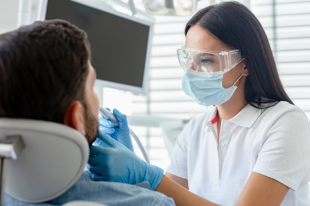 Dentista no procedimento usando broca odontológica para cliente na clínica odontológica moderna