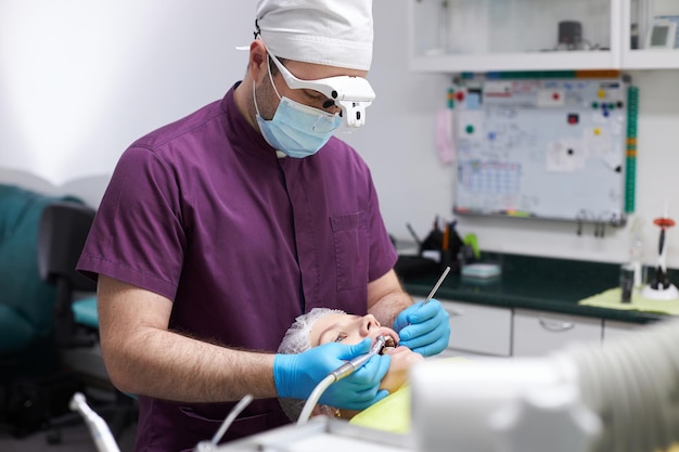 Dentista ortodoncista que usa equipo dental para curar la caries de una paciente joven en la clínica dental