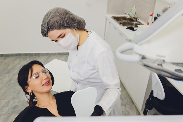 Dentista y paciente eligiendo tratamiento en una consulta con equipo médico en segundo plano