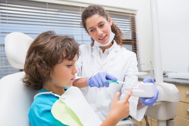 Dentista pediátrica mostrando garotinho como escovar os dentes na clínica odontológica