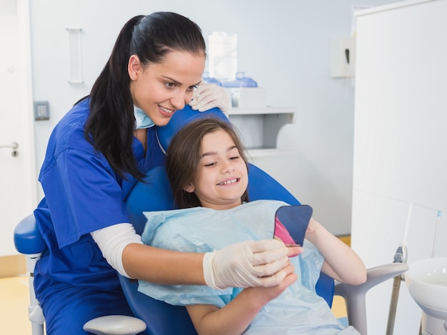 Dentista pediátrico e paciente jovem segurando um espelho