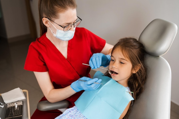 El dentista pediátrico examina la boca y los dientes de la niña y trata los dolores de muelas Paciente infantil feliz de odontología Consulta con el dentista infantil en odontología Tratamiento dental