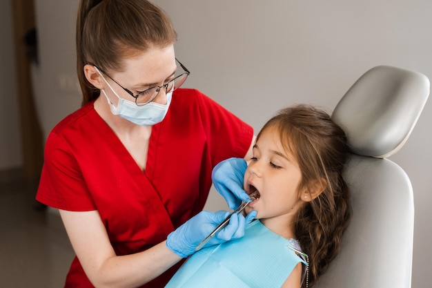 El dentista pediátrico examina la boca y los dientes de la niña y trata los dolores de muelas Paciente infantil feliz de odontología Consulta con el dentista infantil en odontología Tratamiento dental