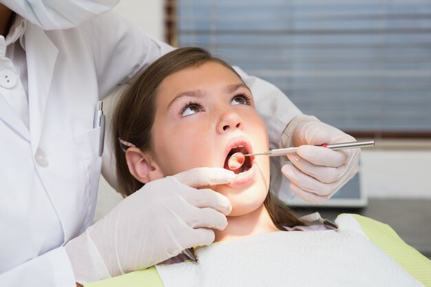 Dentista pediátrico examinando los dientes de una niña en la silla de los dentistas