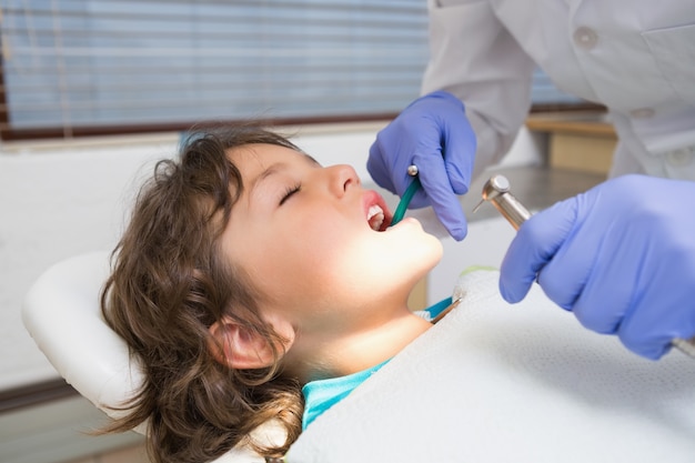 Dentista pediátrico examinando los dientes de un niño pequeño en la silla de dentistas