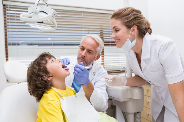 Dentista pediátrico examinando los dientes de un niño pequeño con su asistente