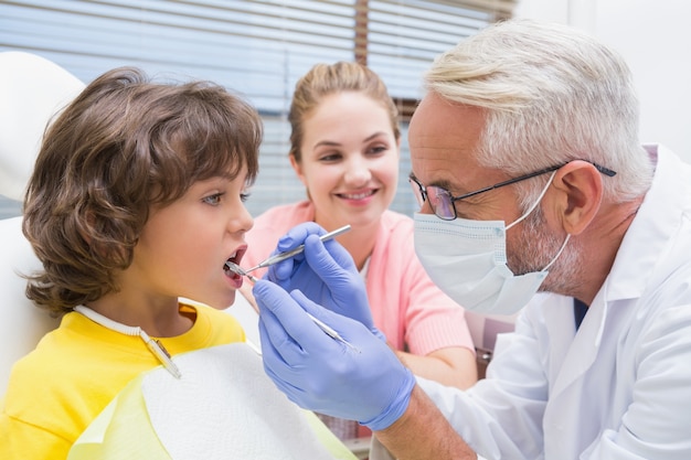 Dentista pediátrico examinar los dientes de un niño pequeño con su madre mirando