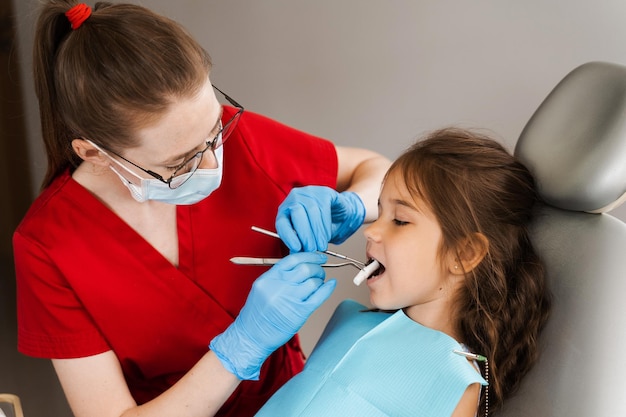 El dentista pediátrico pone un hisopo de algodón en la boca de una niña para instalar un empaste dental de fotopolímero y tratar los dientes