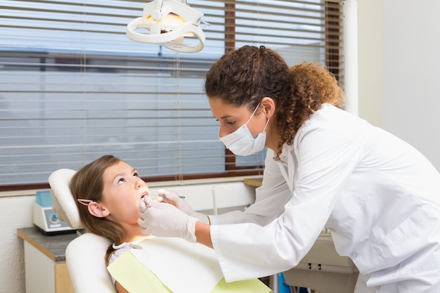 Dentista pediátrico que examina los dientes de un paciente en la silla de los dentistas