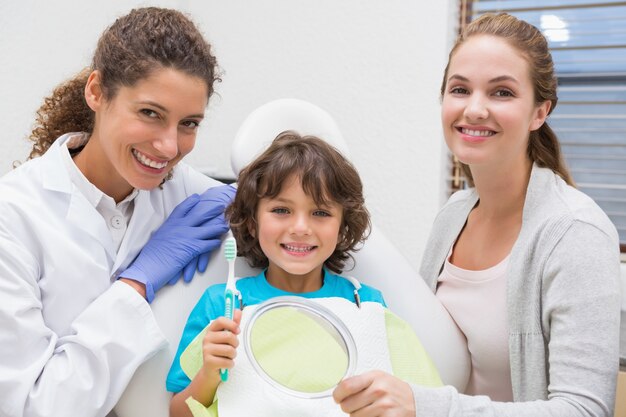 Dentista pediátrico que mostra o menino como escovar os dentes com sua mãe