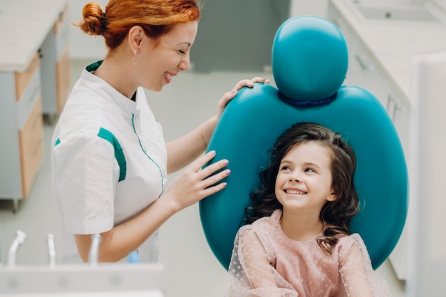 Dentista pediátrico sonriendo mirando a su pequeño paciente. Niña linda sonriendo después del examen dental.