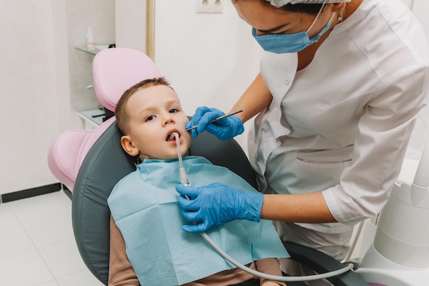 Dentista pediátrico trata cárie infantil e cavidade oral de menino sentado na cadeira do dentista durante check-up médico regular