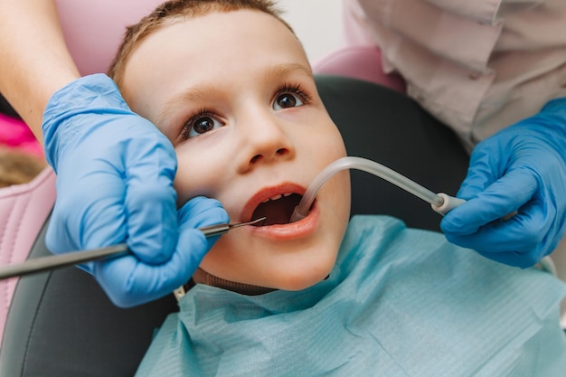 El dentista pediátrico trata la caries infantil y la cavidad bucal del niño sentado en la silla del dentista durante el chequeo médico regular