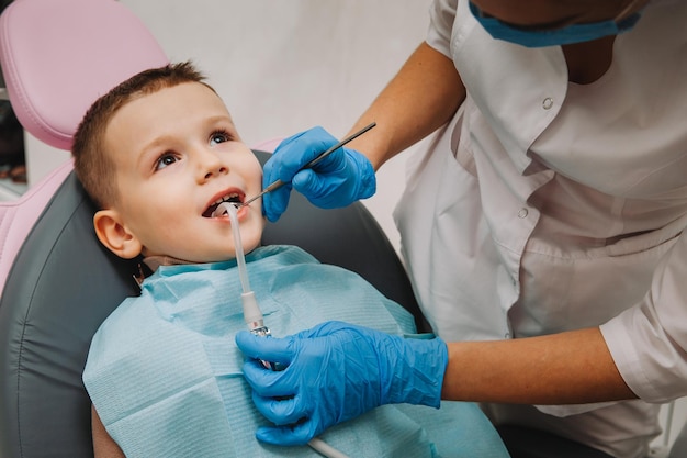 El dentista pediátrico trata la caries infantil y la cavidad bucal del niño sentado en la silla del dentista durante el chequeo médico regular